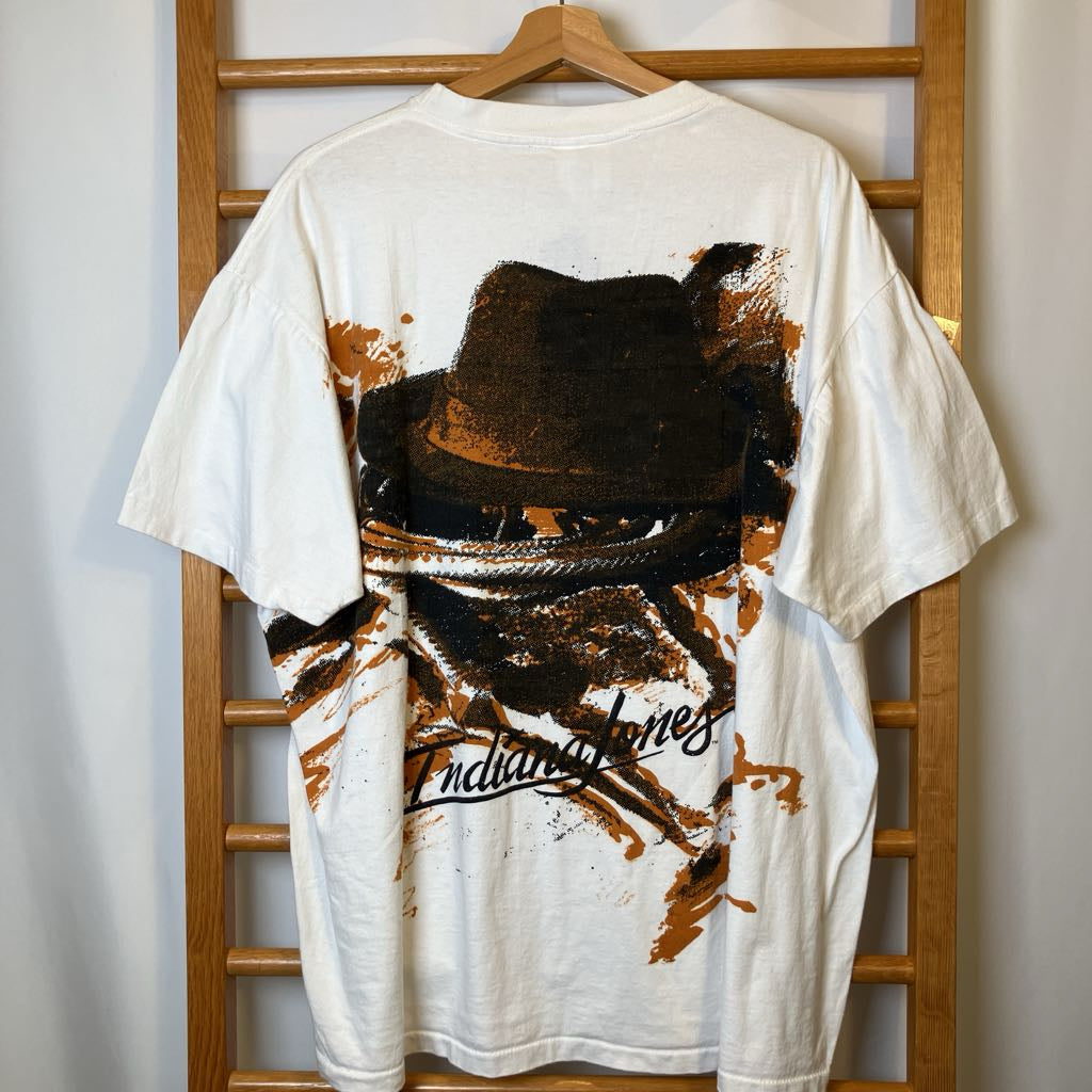 White t-shirt with a graphic design of a hat and text on a wooden hanger against a white wall.