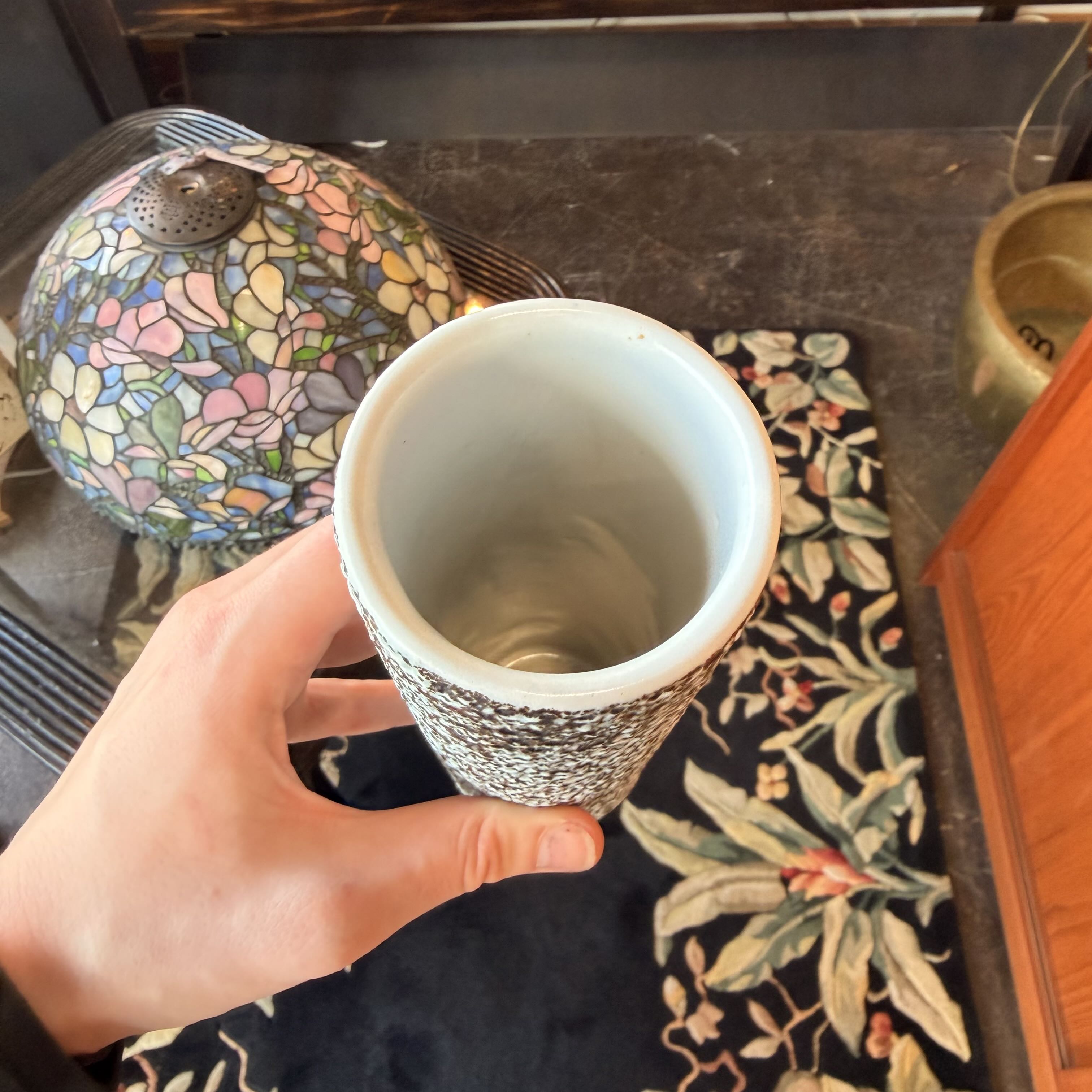 Hand holding a textured ceramic cup on a kitchen counter with a decorative mat and container in the background.