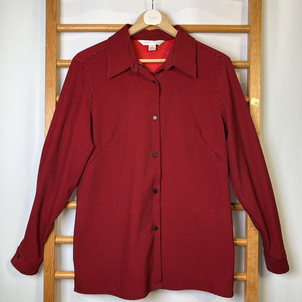 Red checkered shirt on a hanger against a white wall with wooden rack.
