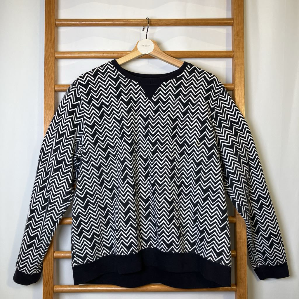 Black and white zigzag patterned sweater on a wooden hanger against a white wall.