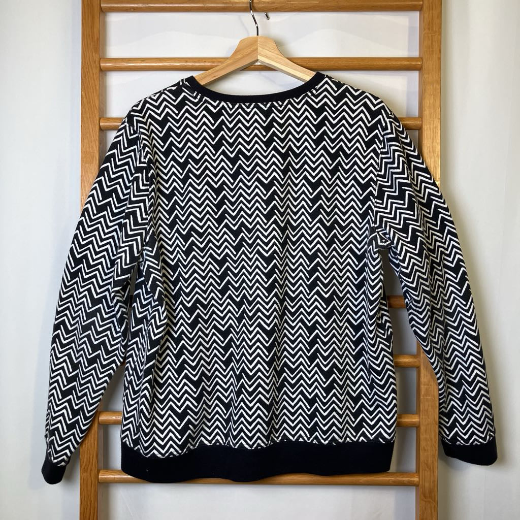 Black and white zigzag patterned sweater on a wooden hanger against a white wall.