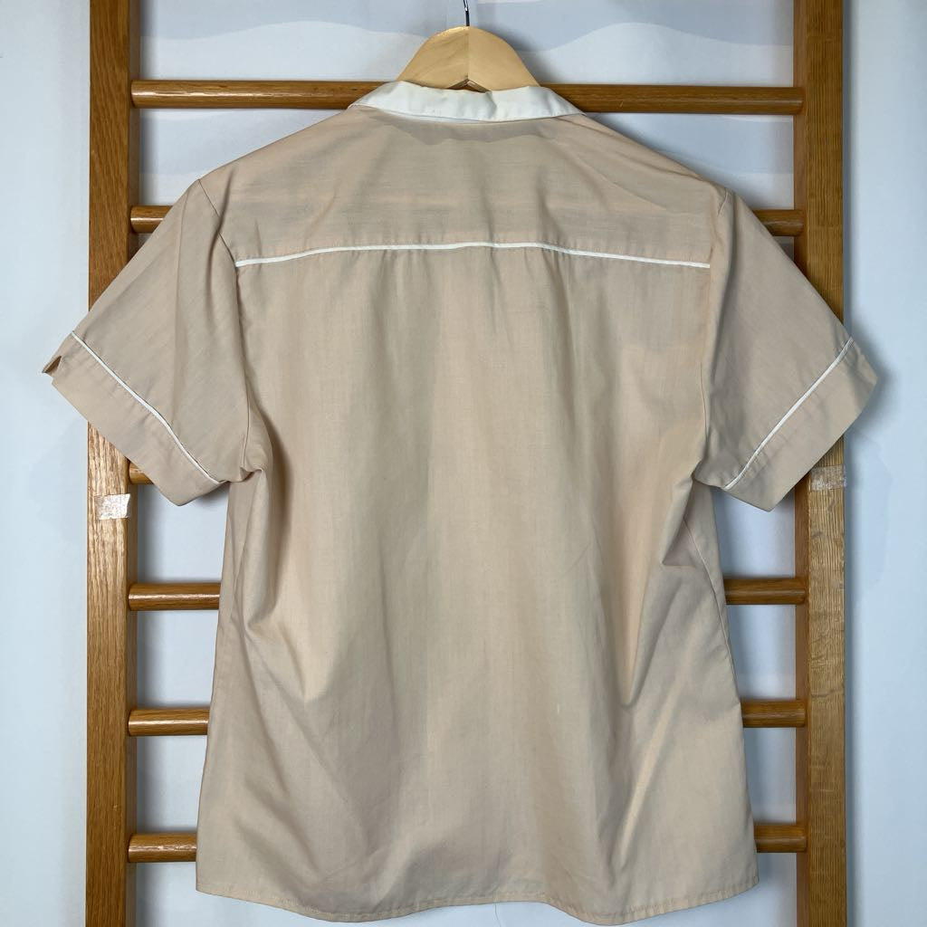 Beige shirt with white trim on a hanger against a white wall