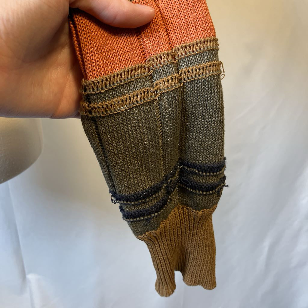 Hand holding a knitted item with orange, brown, and black colors on a white background