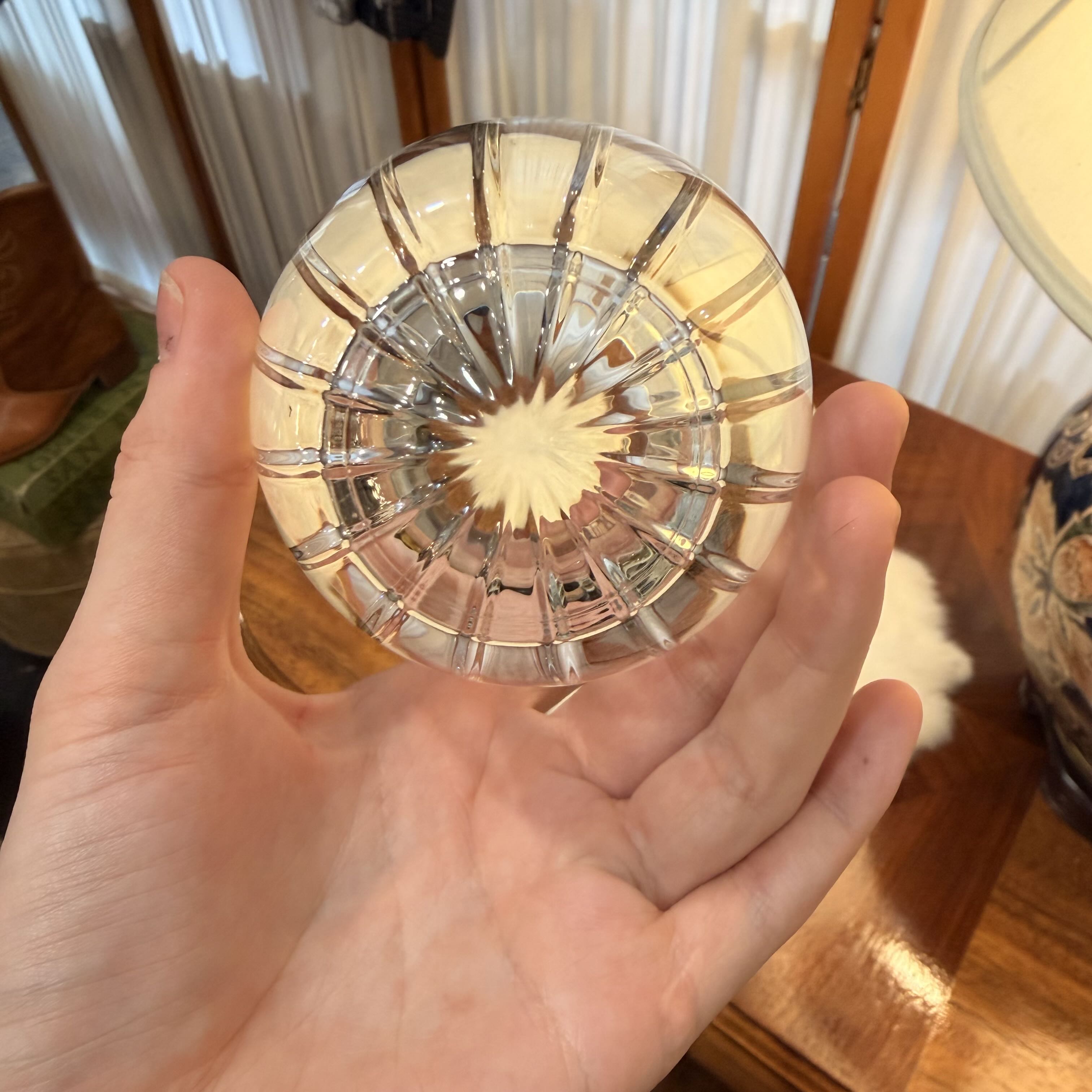 Hand holding a clear glass ornament with a wooden floor and chair in the background