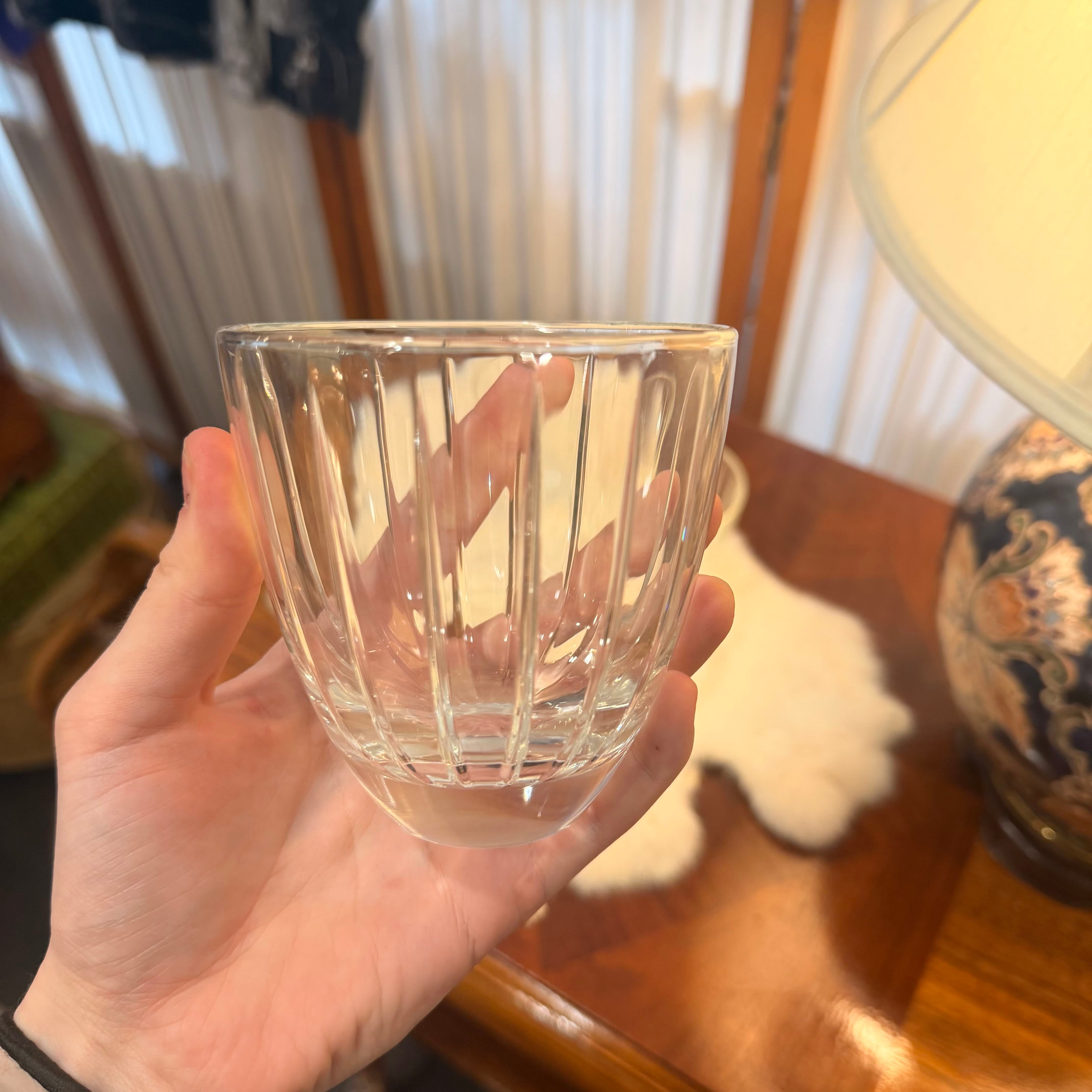 Hand holding a clear glass with vertical ridges, blurred indoor background