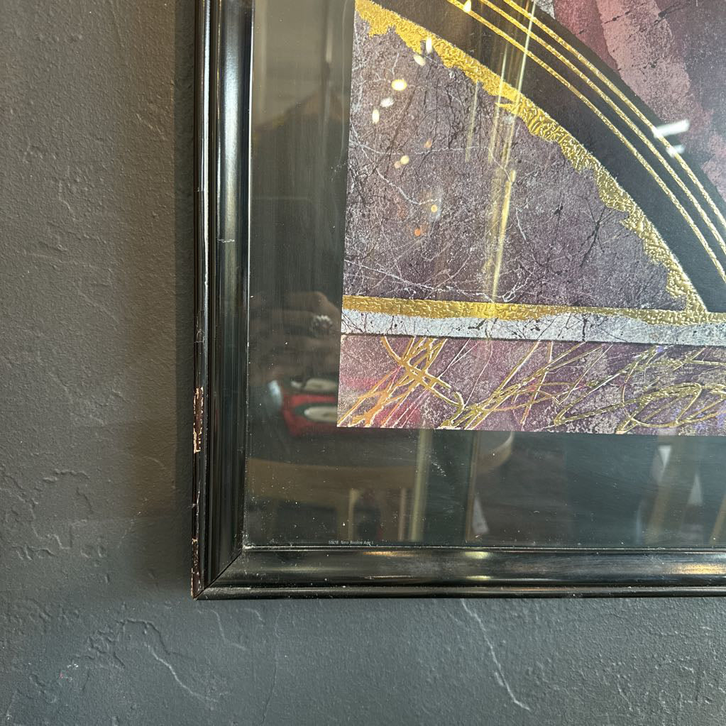 Framed artwork with a textured surface and gold accents on a gray wall.