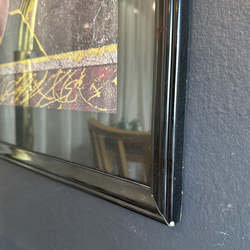 Framed artwork on a wall with a mirror reflecting a room.