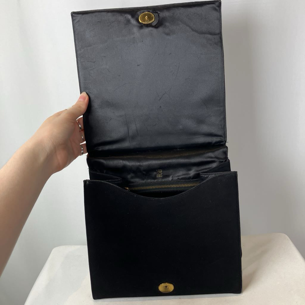 Black clutch bag with gold clasp held open by a hand on a white background
