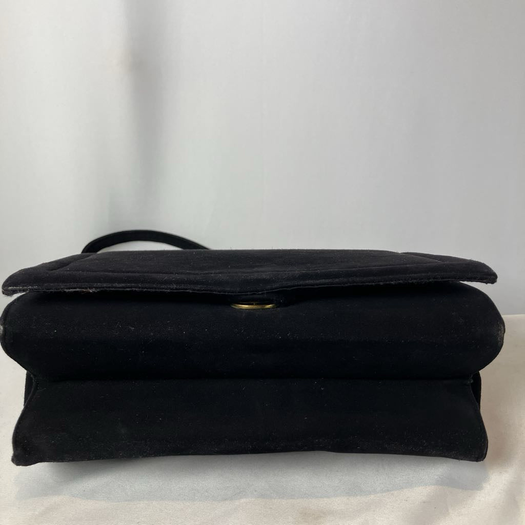 Bottom of a black purse on a white surface with a light gray curtain background