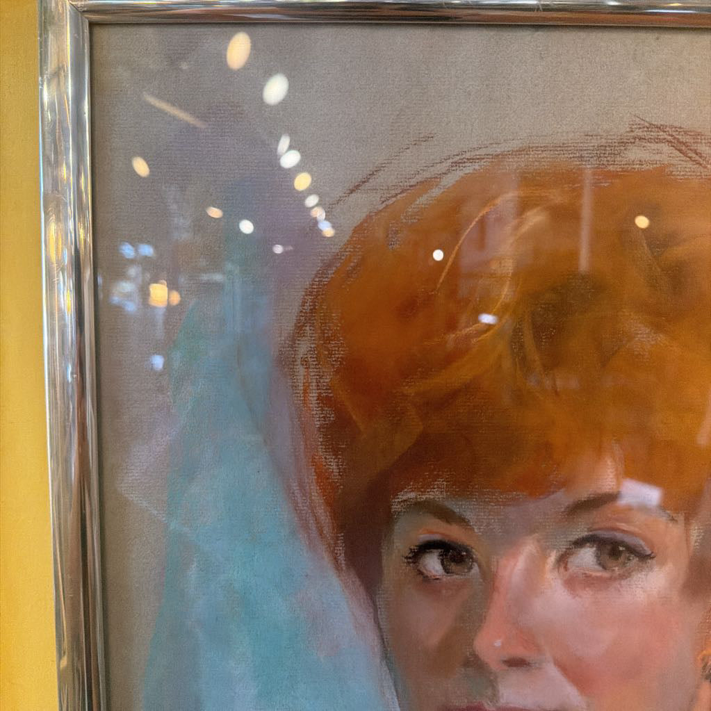 Close-up of a painting of a woman with red hair and a blue dress, framed in silver.
