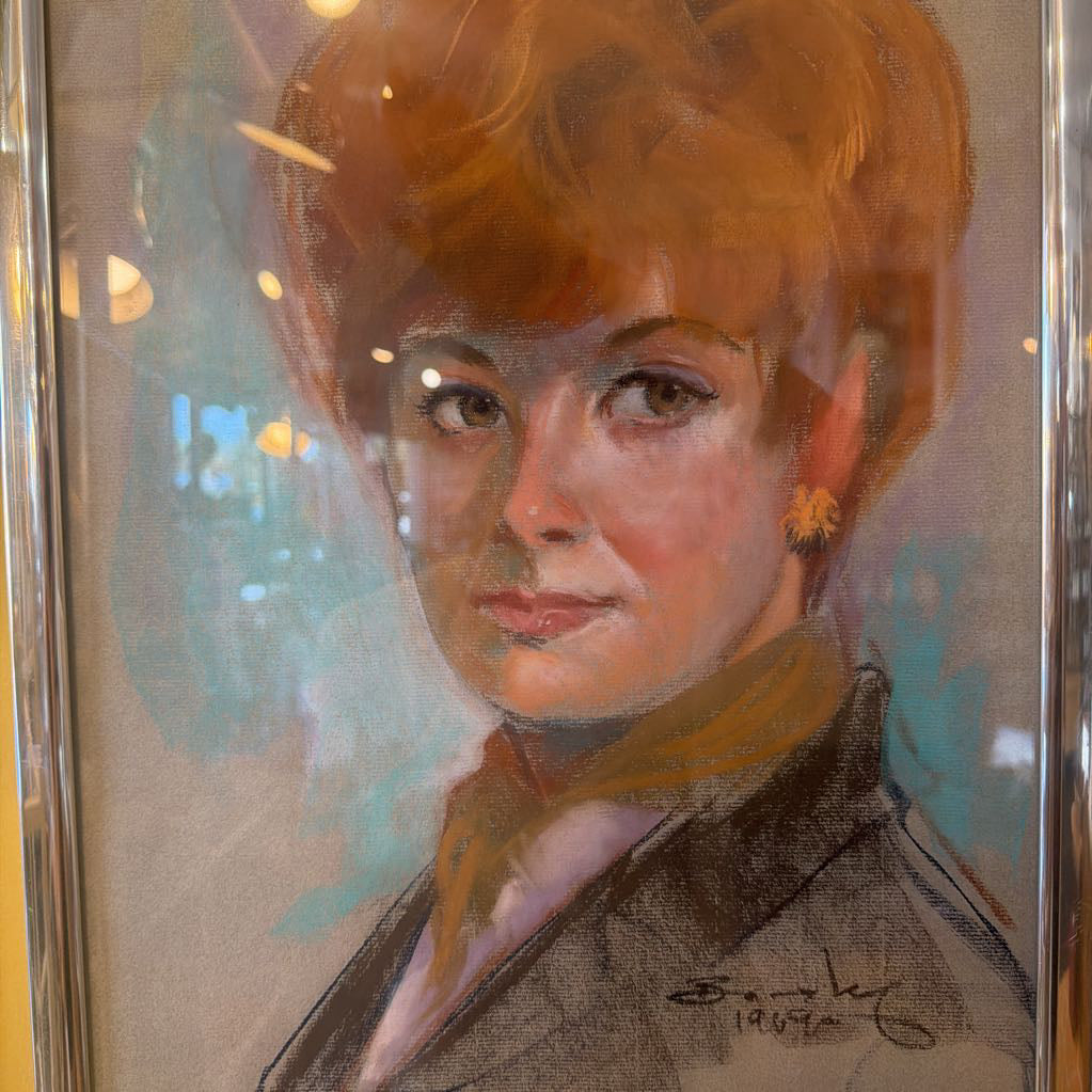 Framed portrait of a woman with red hair and a brown jacket.