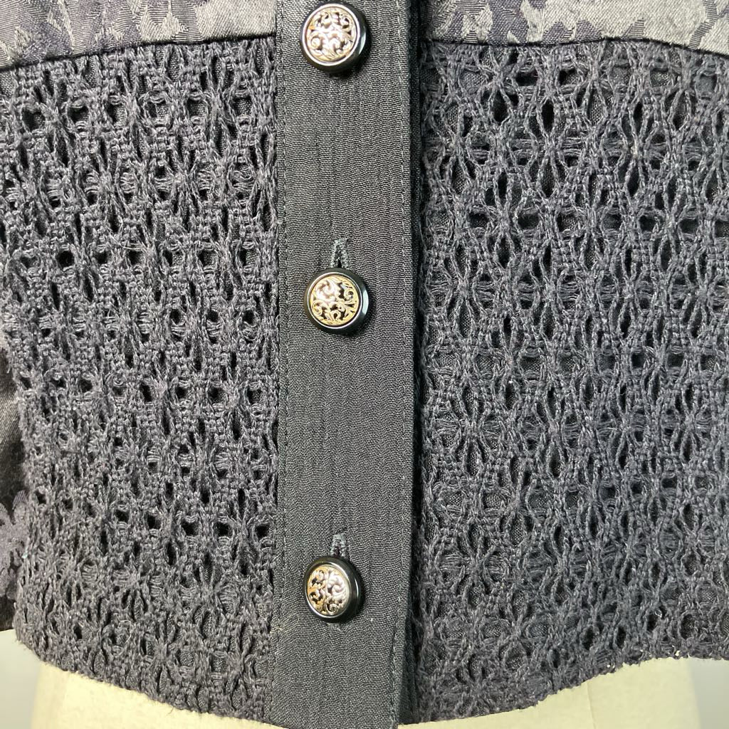 Close-up of a black textured garment with decorative buttons on a mannequin.