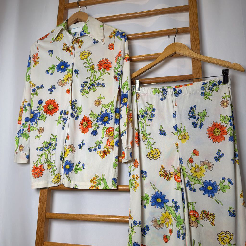 Floral-patterned shirt and pants hanging on a wooden rack against a white wall.