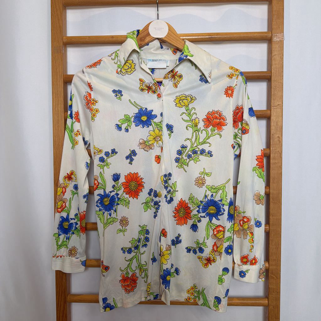 Colorful floral-patterned shirt on a wooden rack against a white wall