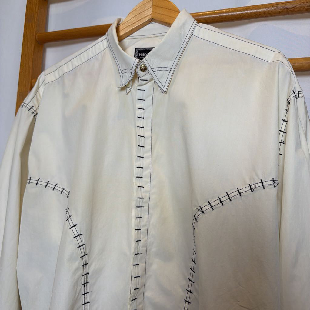 White shirt with black stitching on a wooden hanger against a white wall.