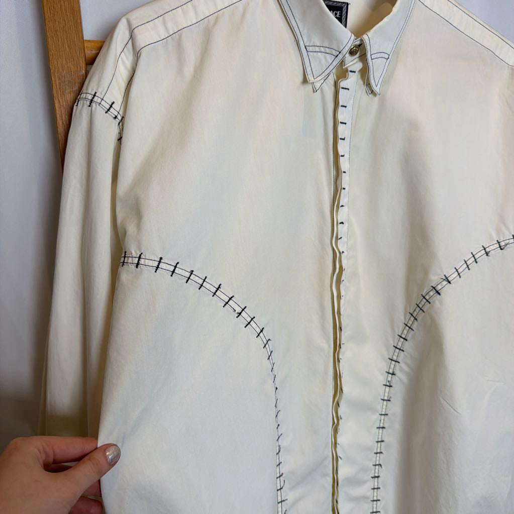 White shirt with black stitching held by a hand against a neutral background