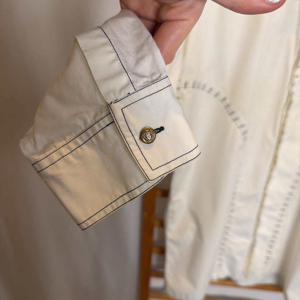 Close-up of a white shirt cuff with a button, held by a hand against a neutral background.