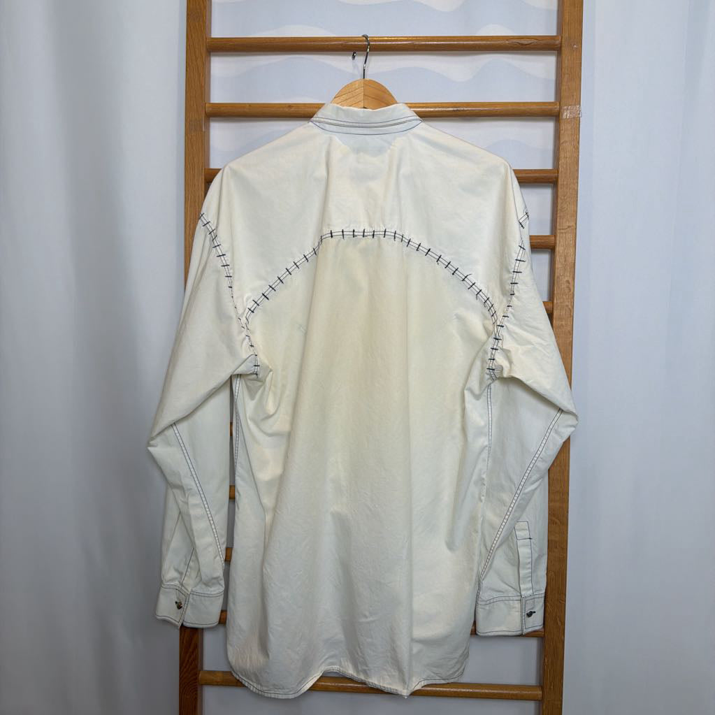 White shirt with black stitching on a wooden rack against a white wall