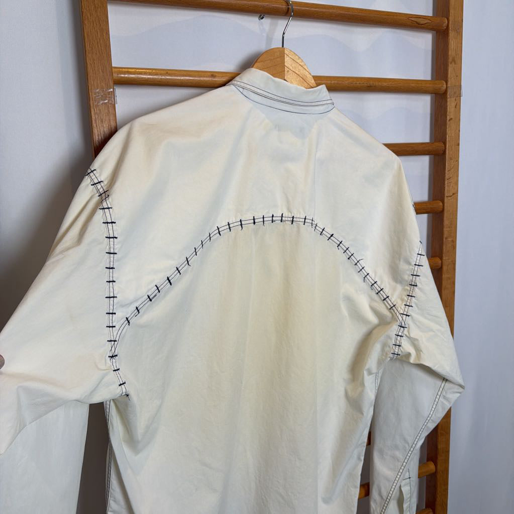 White shirt with black stitching on a wooden hanger against a white wall
