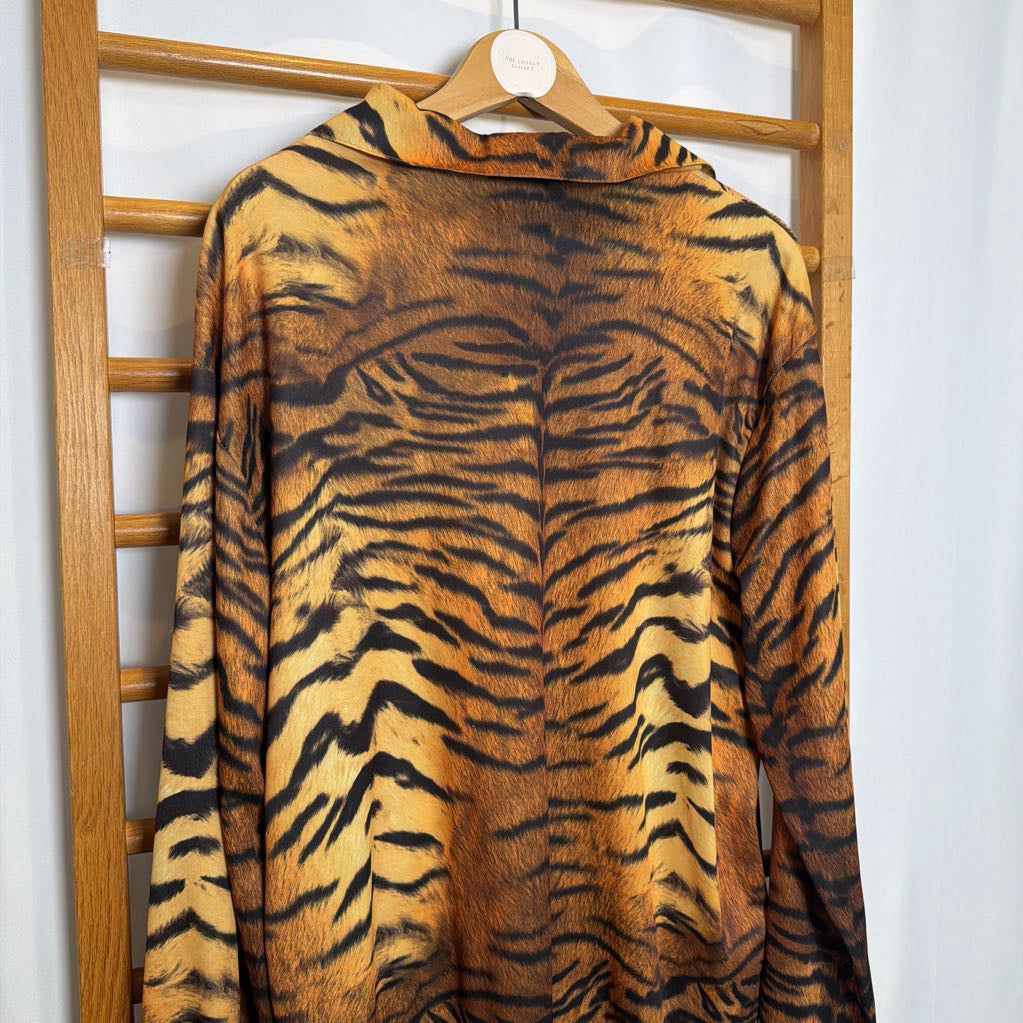 Tiger-striped sweater on a wooden hanger against a white wall