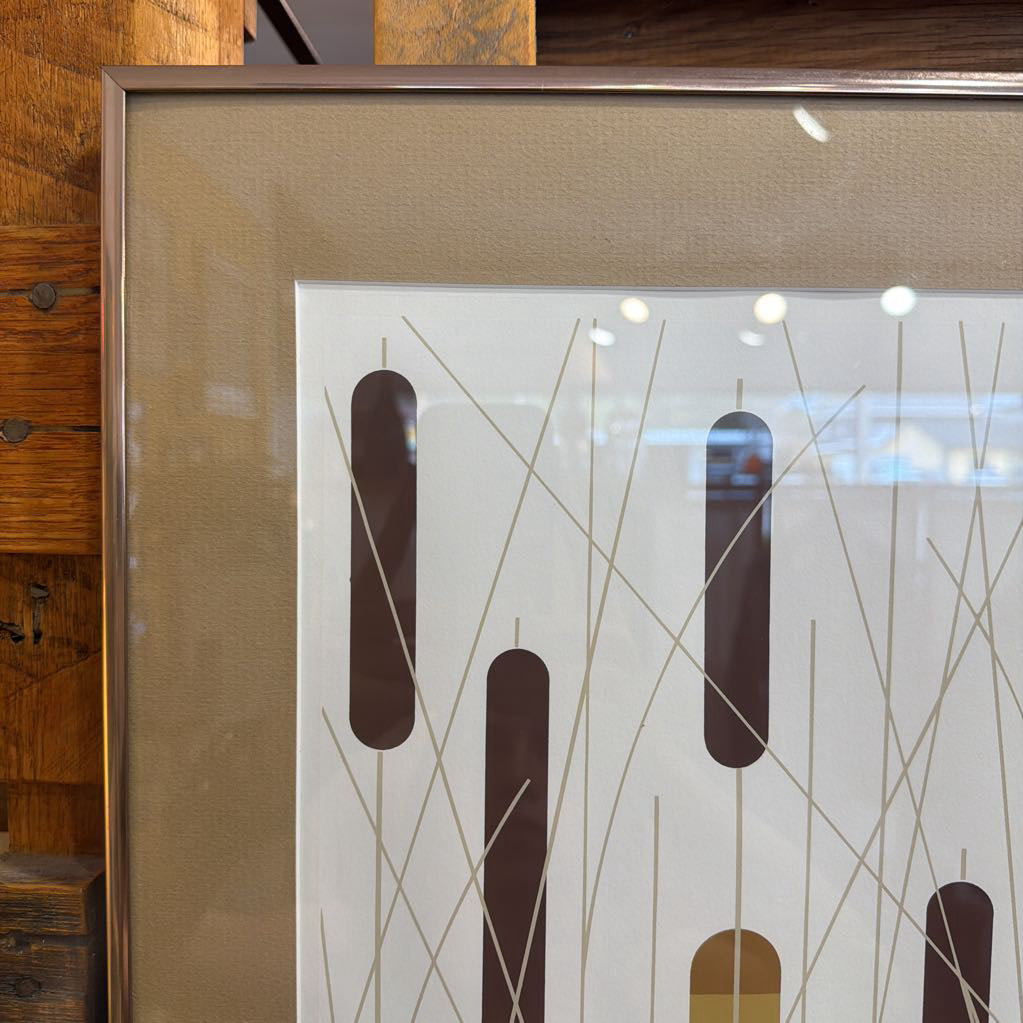 Framed abstract artwork with brown and beige shapes on a wooden surface