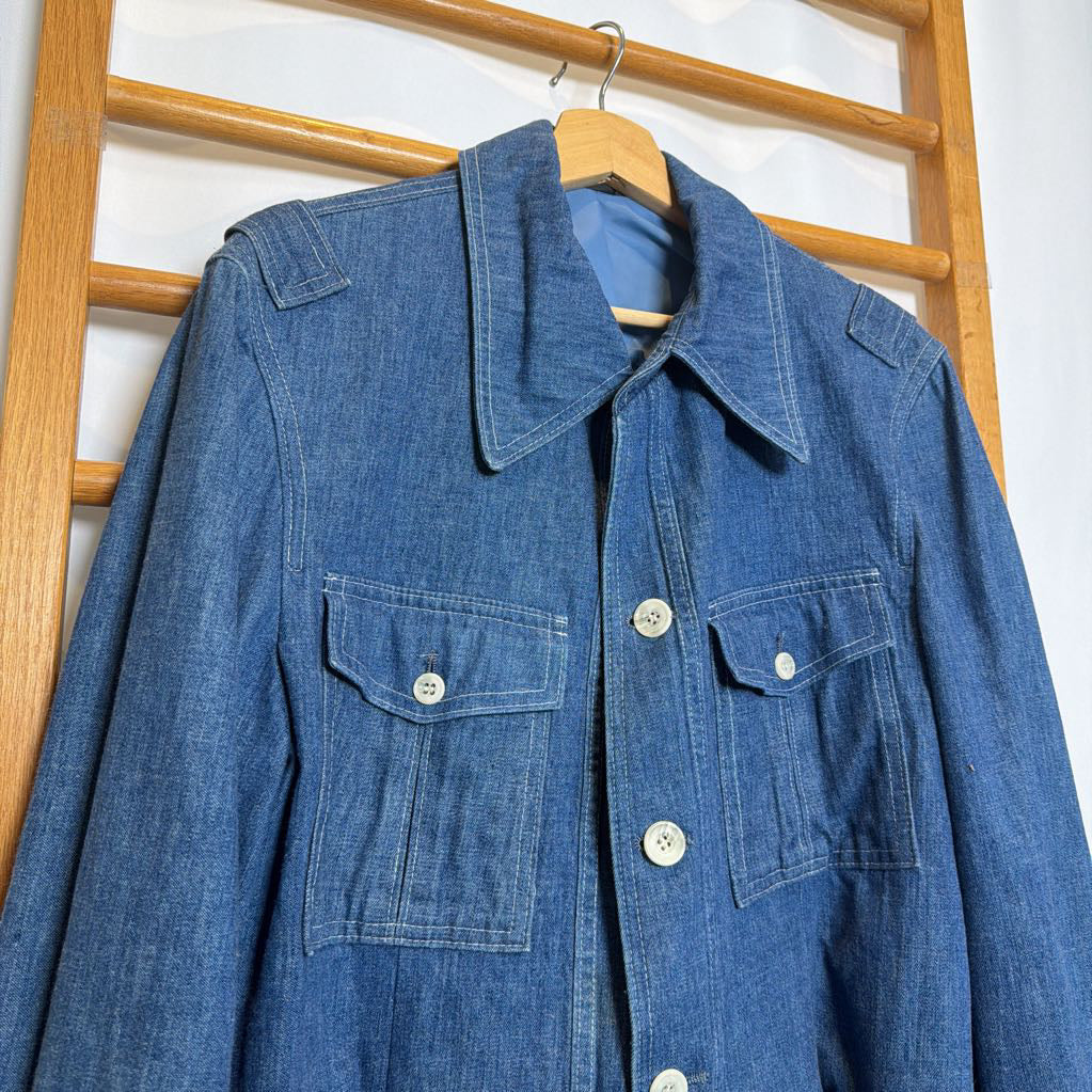 Blue denim jacket on a wooden hanger against a white wall.