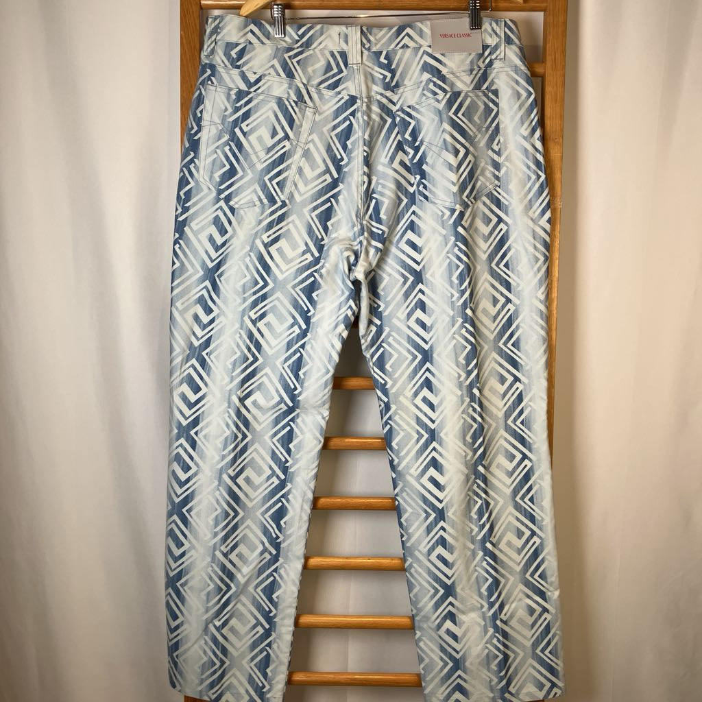 Blue and white patterned pants hanging on a wooden hanger against a beige curtain background