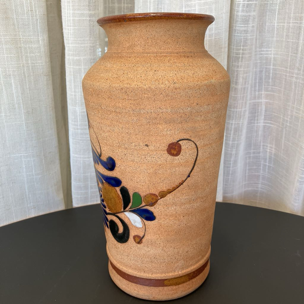 Ceramic vase with decorative elements on a dark surface and light curtain background