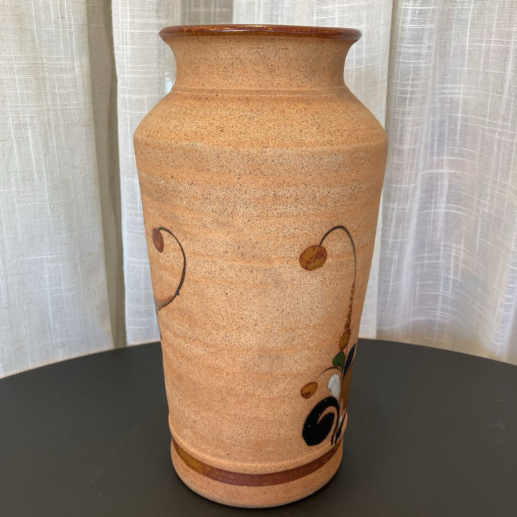 Ceramic vase with decorative elements on a dark surface and light curtain background
