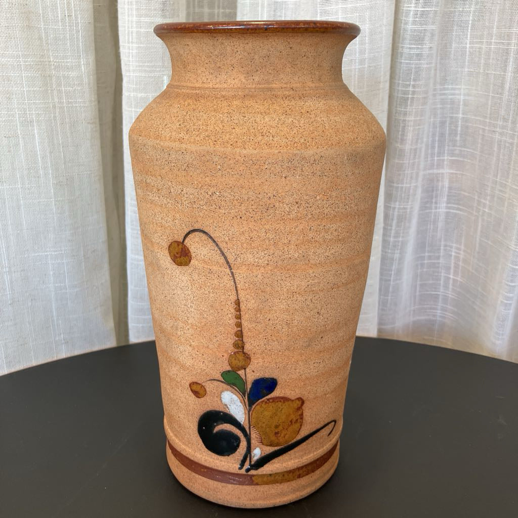 Ceramic vase with decorative elements on a dark surface and light curtain background