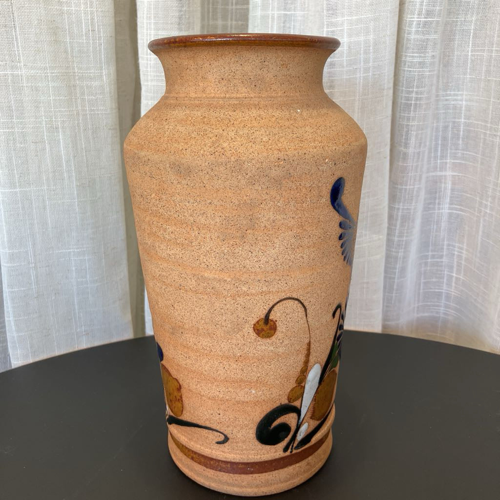 Beige ceramic vase with black floral design on a dark surface with a light curtain background