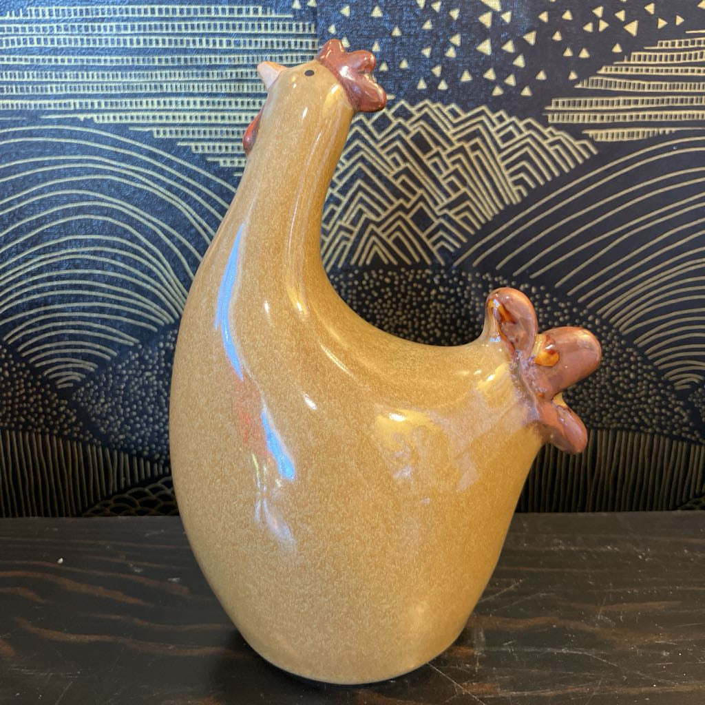 Ceramic chicken figurine on a dark surface with a patterned blue background