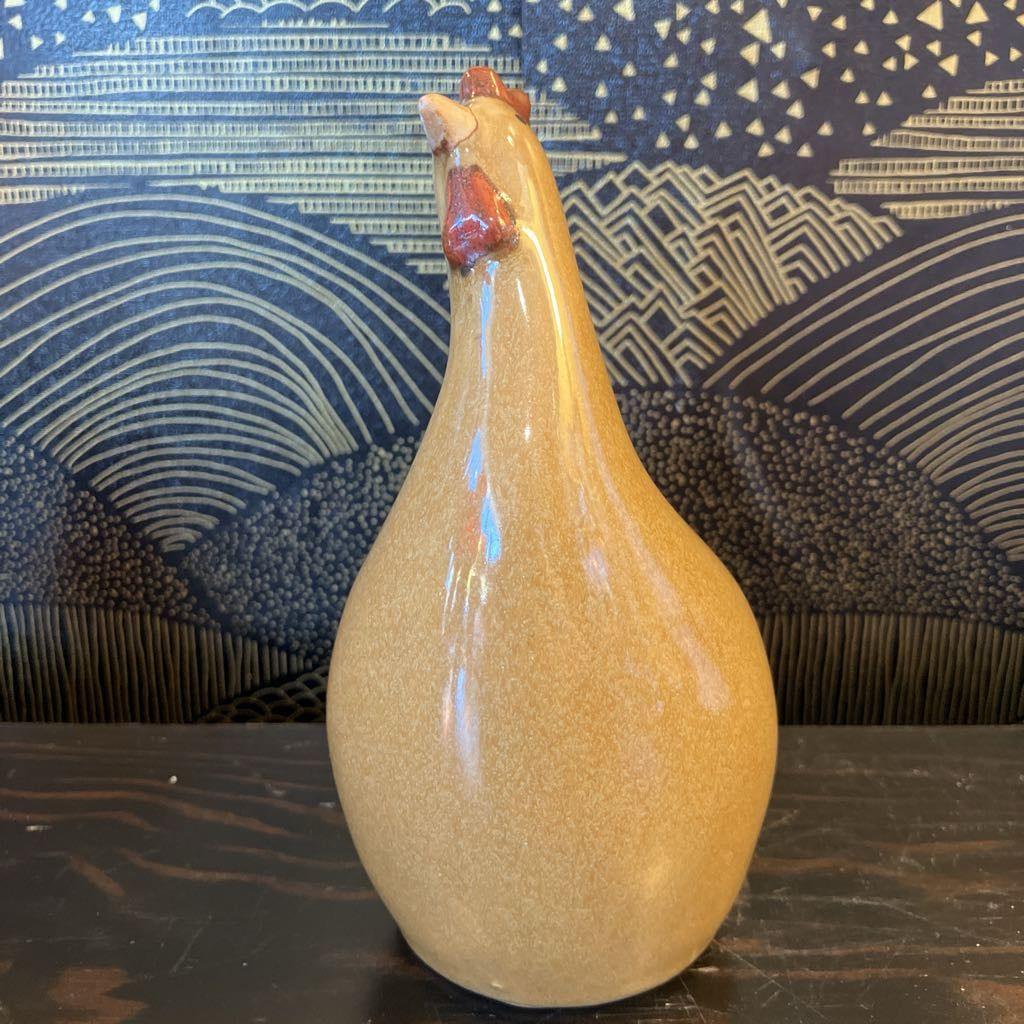 Beige ceramic chicken figurine with a textured surface on a dark surface with a patterned blue background