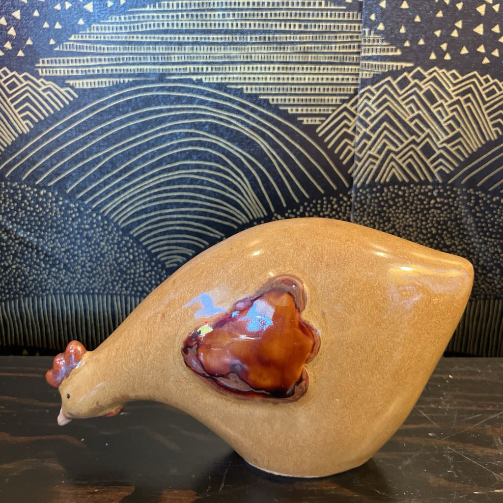 Ceramic chicken figurine with a glossy finish on a dark surface with a patterned background
