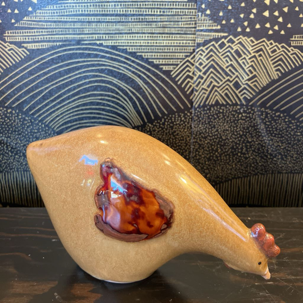 Ceramic chicken figure with a dark interior against a patterned wall.