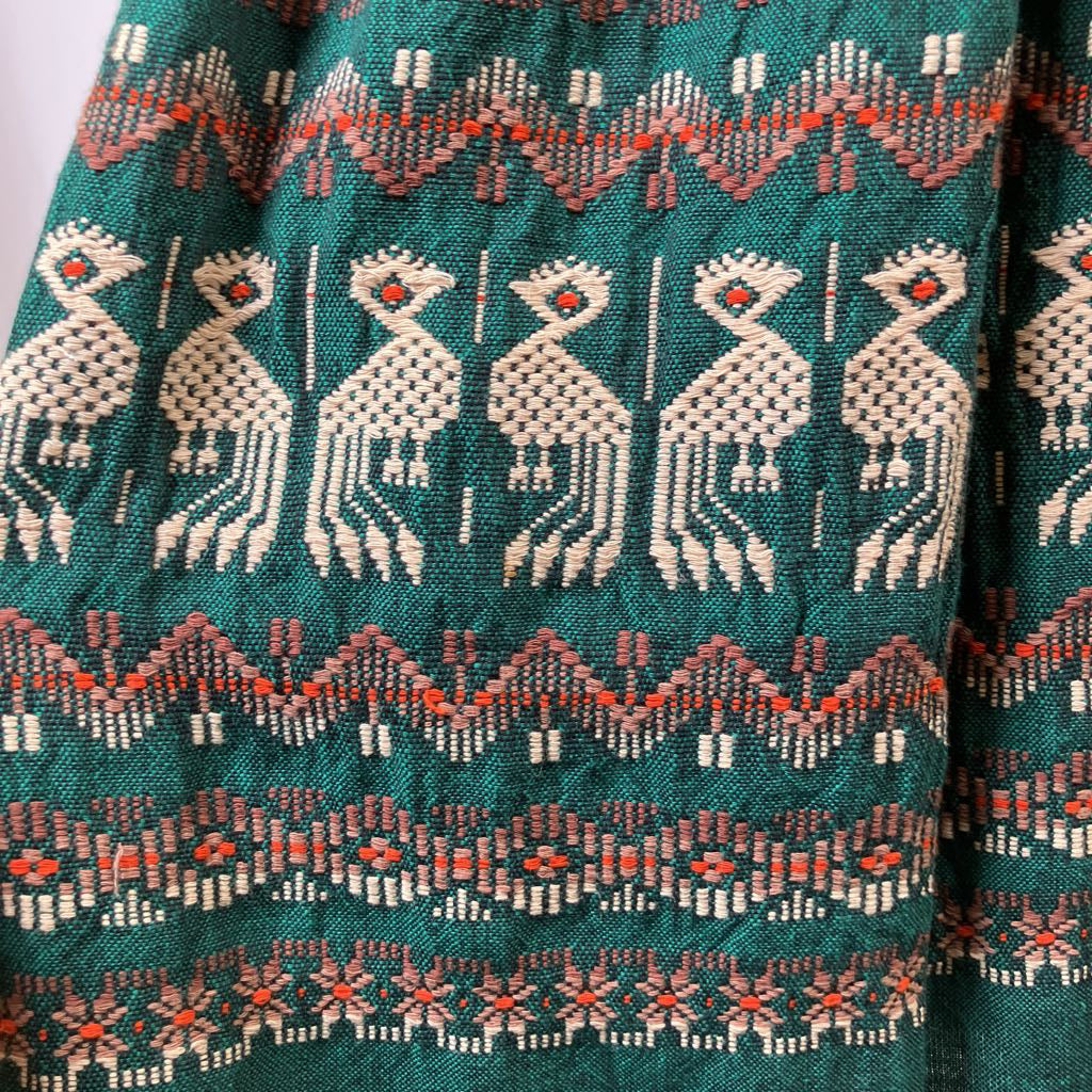 Close-up of a fabric with intricate patterns and animal-like figures on a teal background.