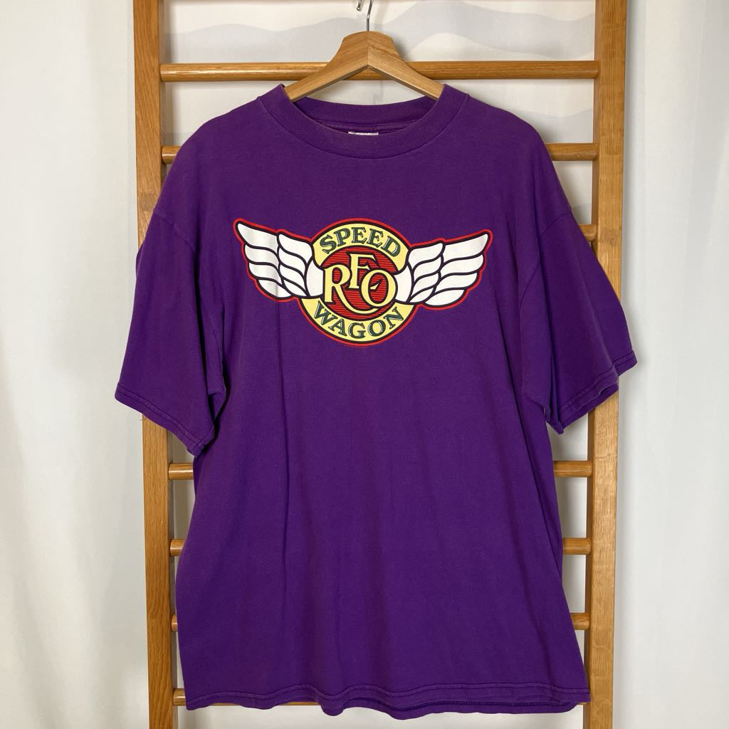Purple t-shirt with a logo on a wooden hanger against a white wall