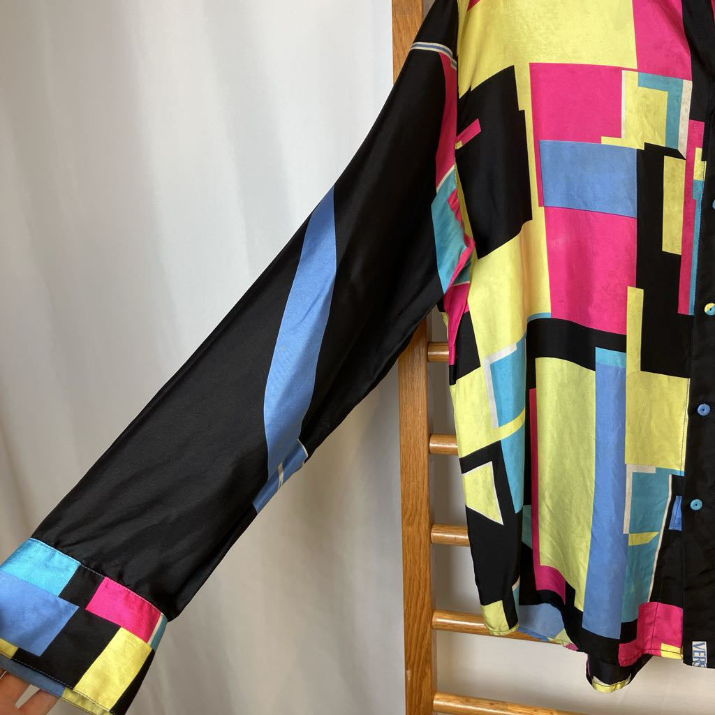 Colorful geometric-patterned shirt hanging on a wooden rack against a white background