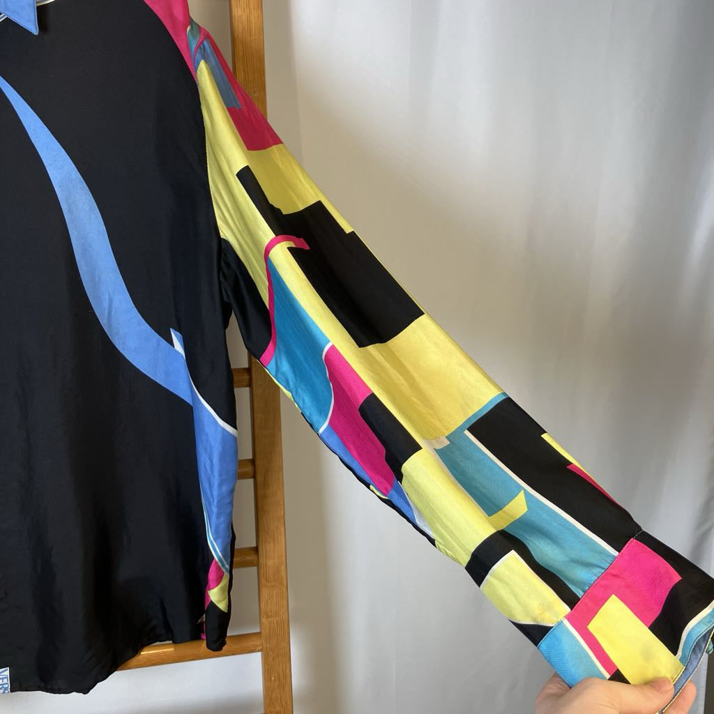 Colorful geometric-patterned shirt held by a person against a neutral background