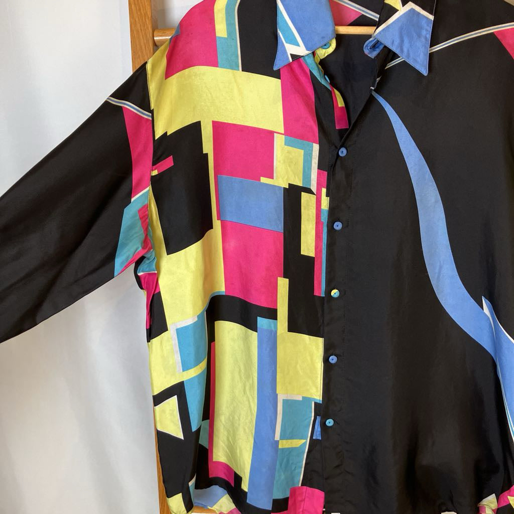 Colorful geometric-patterned shirt over a black shirt on a wooden hanger.