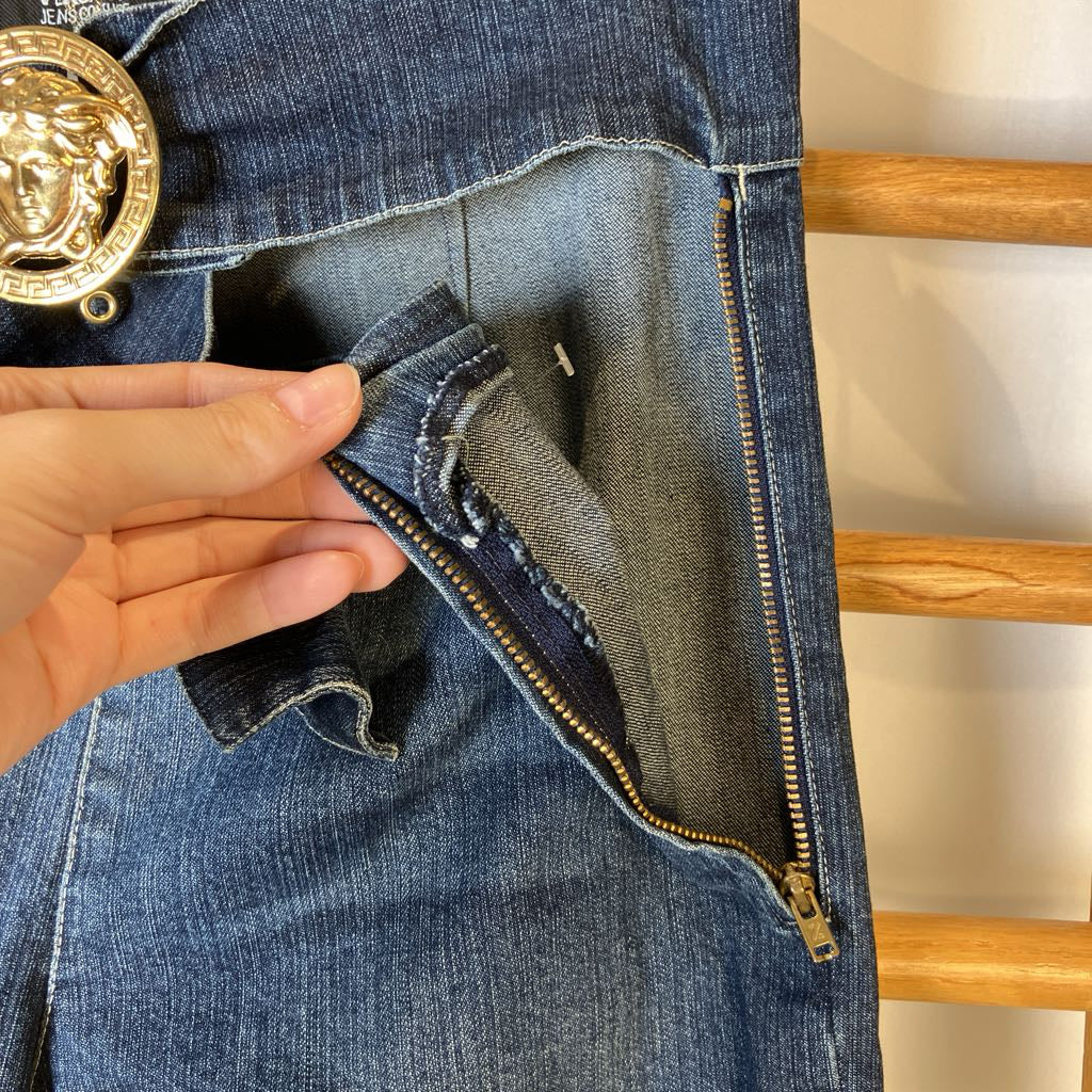 Close-up of blue jeans with a gold zipper and decorative button on a wooden hanger.