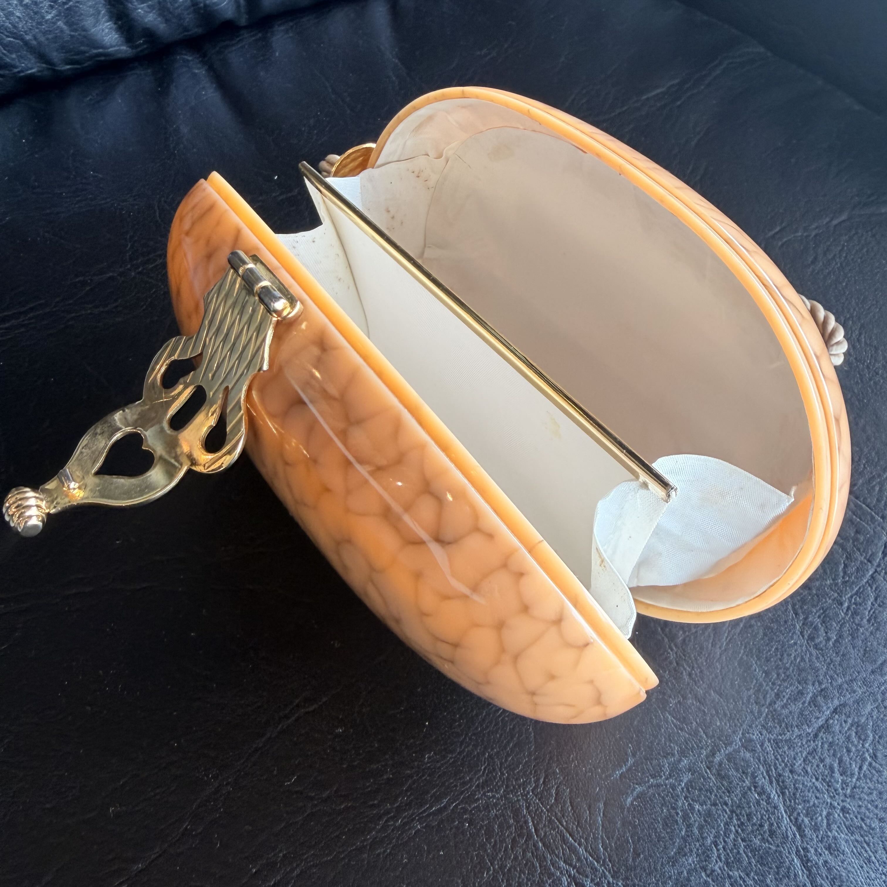 Open beige jewelry box with a gold clasp on a dark surface