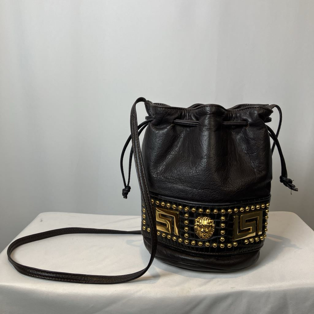 Black leather bucket bag with gold studs on a white surface