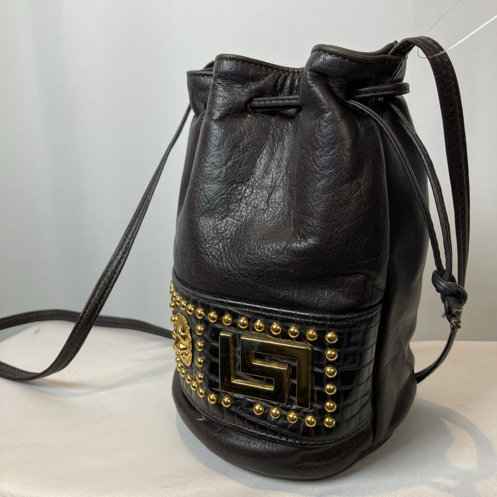 Black leather drawstring bag with gold studded detailing on a light gray background