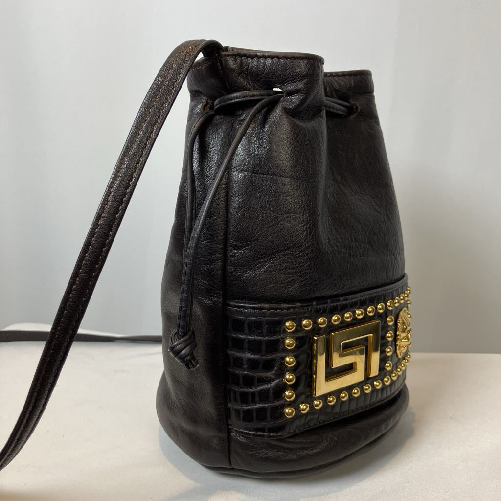 Black leather bucket bag with gold studs on a light gray background