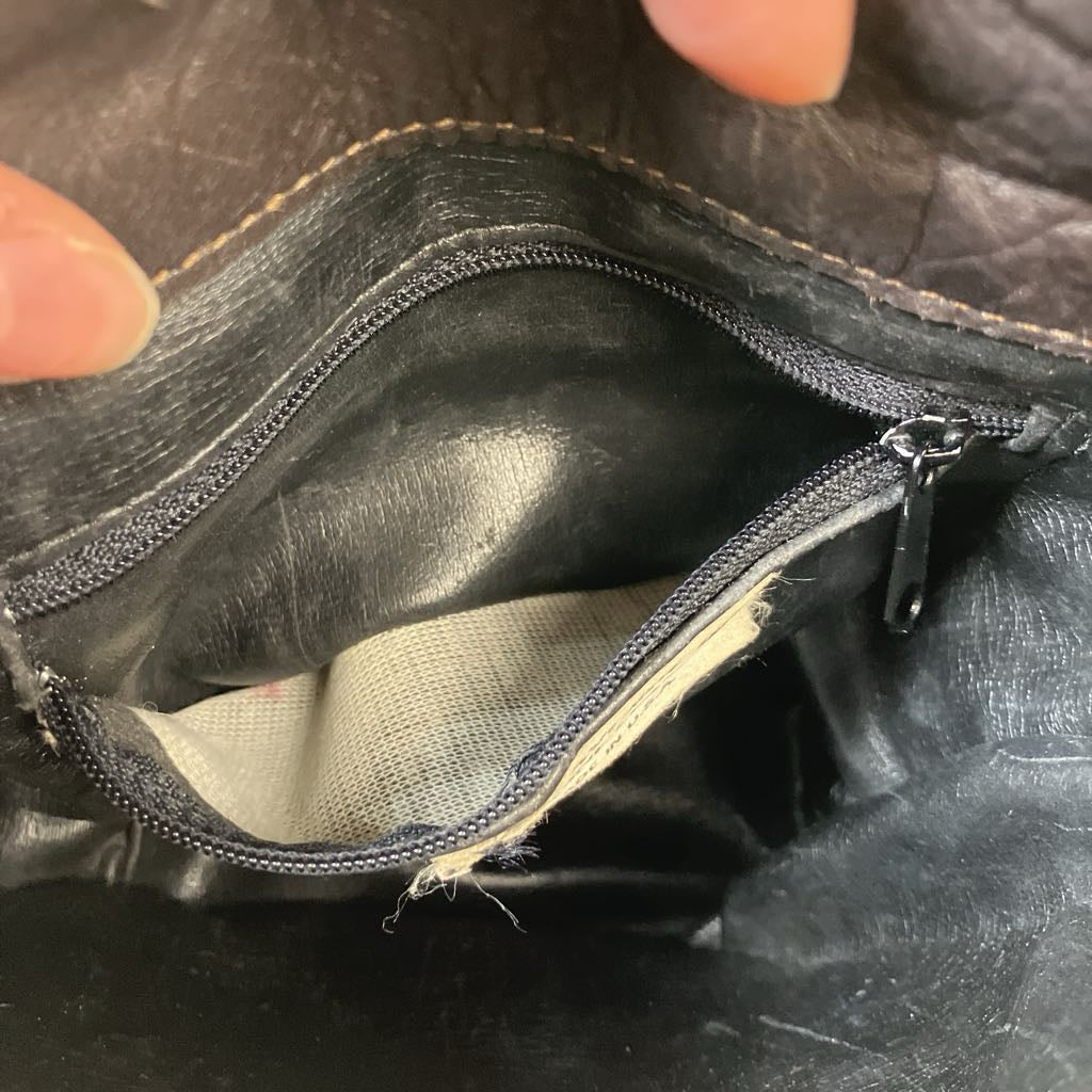 Close-up of a black leather pouch with a zipper, held by a hand.