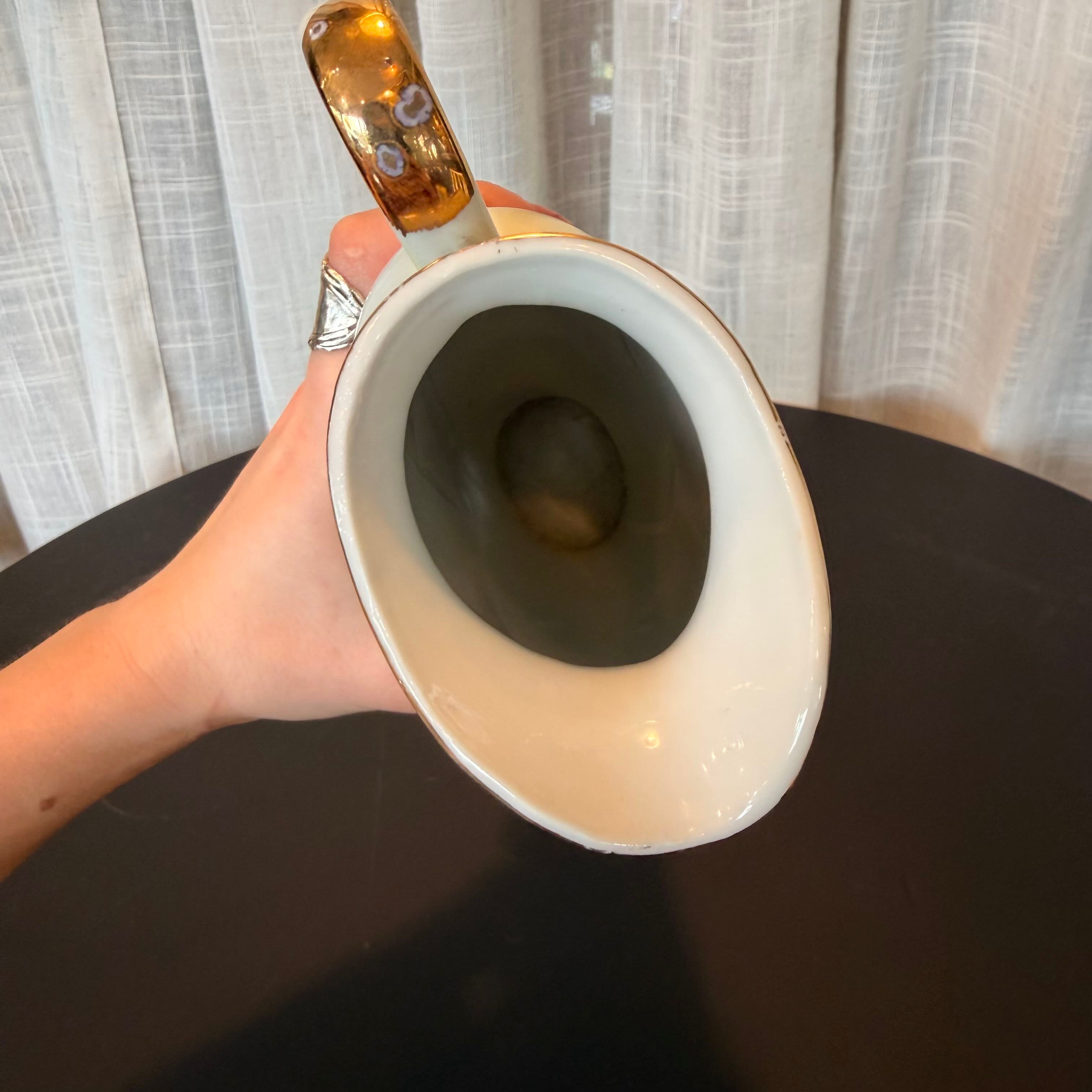 Hand holding a white ceramic mug with a gold handle against a neutral background