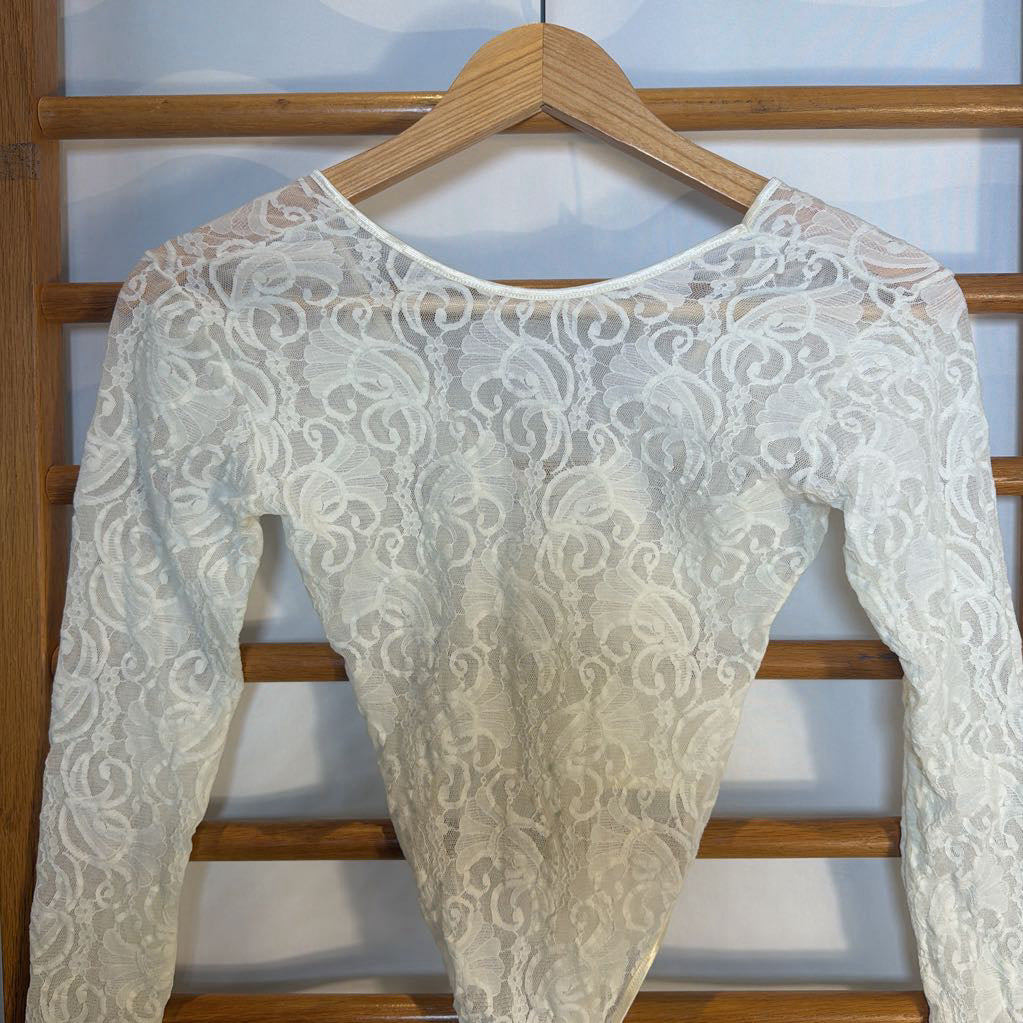 White lace top on a wooden hanger against a white wall.