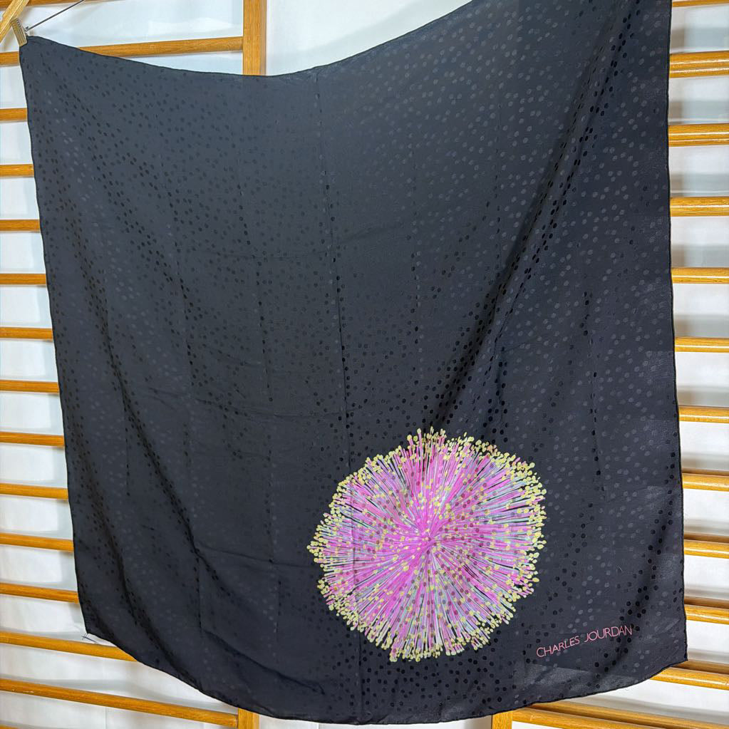 Black scarf with a pink and gold floral design on a wooden and white striped background