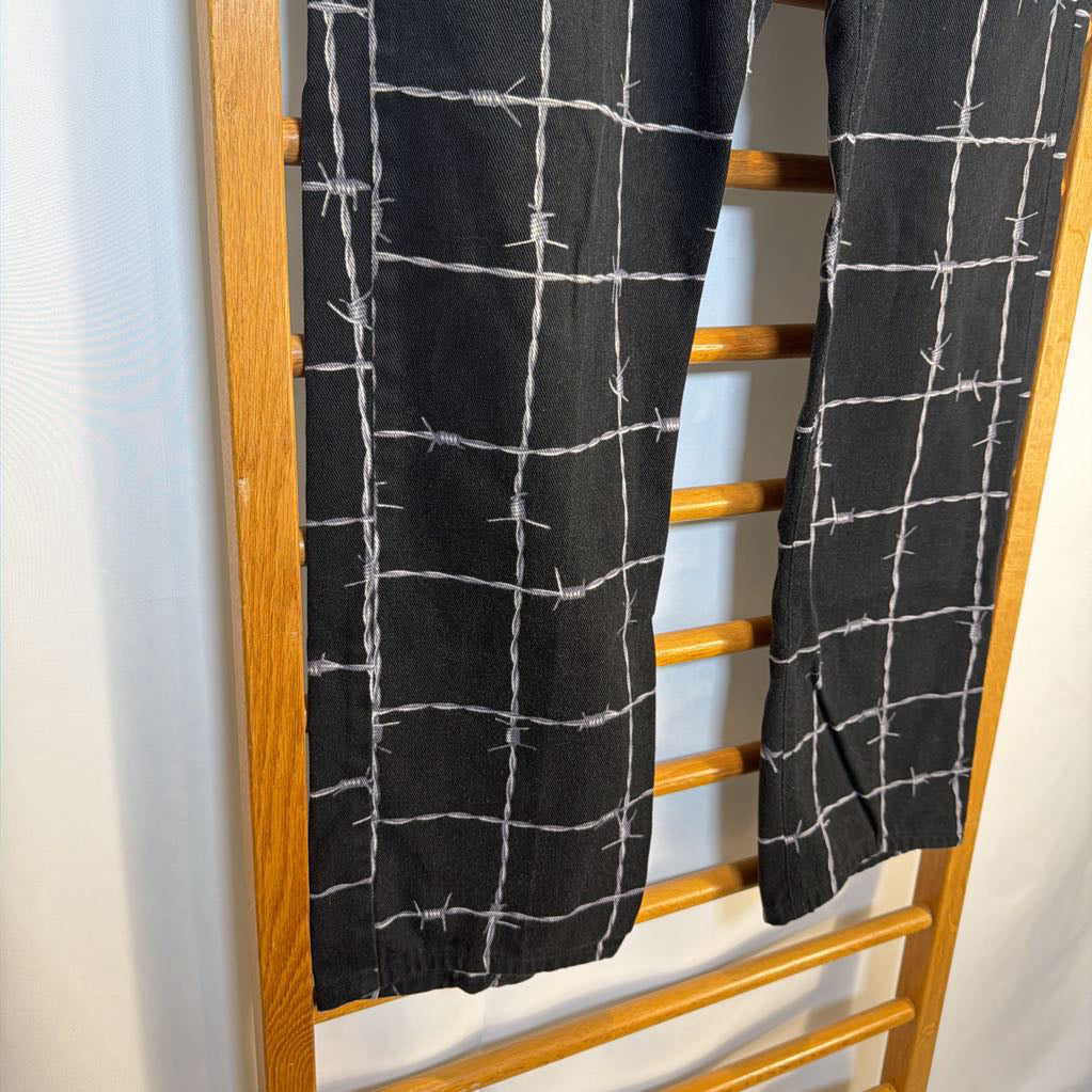 Black pants with white grid pattern hanging on a wooden rack.